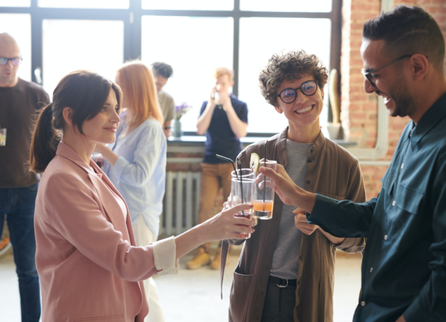 Duas mulheres e um homem conversam e brindam com copos de sumo enquanto fazem networking.