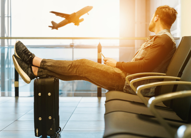 Jovem sentado no aeroporto, com os pés sobre a mala, antes de ir estudar no estrangeiro.