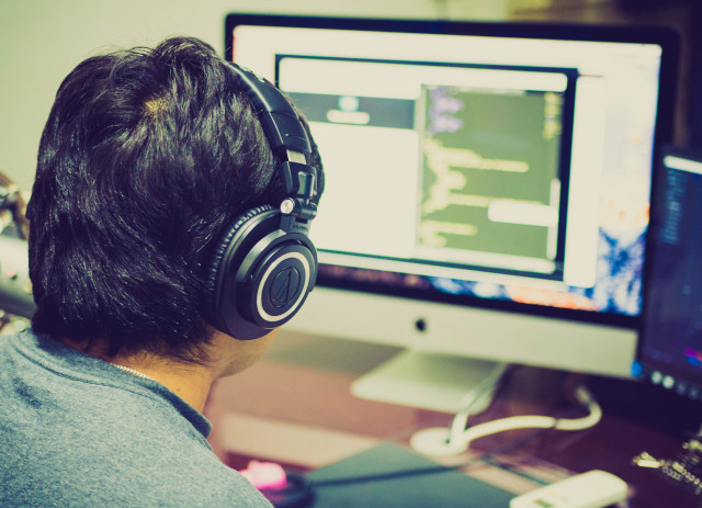 Homem com phones olha para computador a pensar na diferença entre TI vs Telecomunucações vs Engenharia Informática