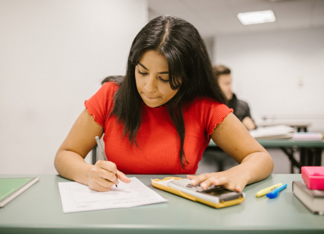 Estudante feminina de camisola laranja a fazer Exames Nacionais do Secundário.