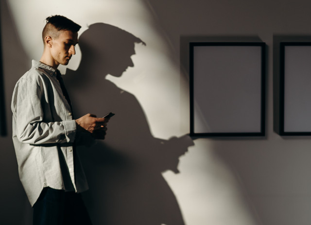 Candidato fantasma com telemóvel na mão e a sua sombra na parede é exemplo de ghosting no emprego.