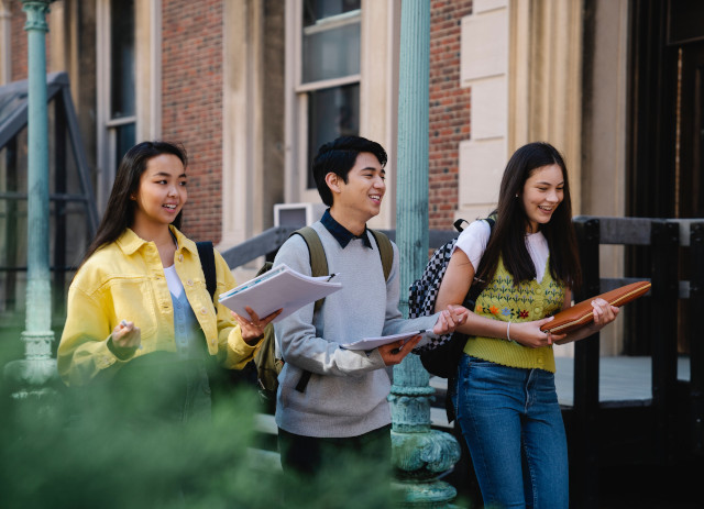 Três jovens estudantes caminham na rua, sorrindo, e conversam sobre as melhores universidades portuguesas.