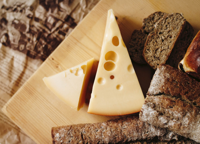Um queijo com bolhas ao lado de pão castanho numa tábua de madeira é um exemplo de como a música pode mudar o sabor do queijo.