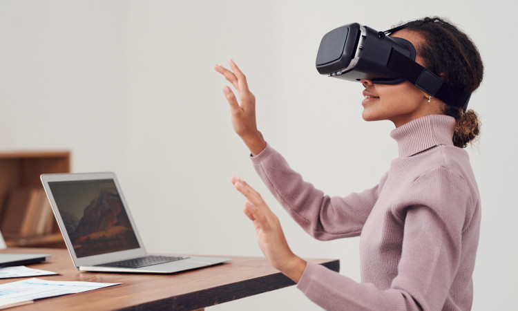Jovem mulher de camisola rosa, com óculos de realidade virtual e braços a tactear o ar, frente a um computador num dos trabalhos online mais estranhos.