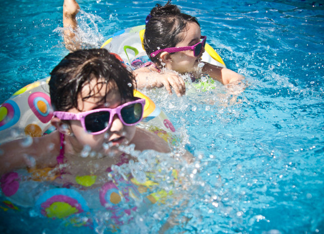 Duas meninas de óculos e boias a nadar numa piscina durante natação, um dos exemplos de atividades extracurriculares.