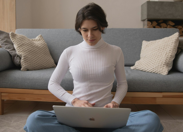 Mulher jovem com o cabelo apanhado, camisola branca e calças de ganga azuis, sentada no chão da sala a fazer uma análise SWOT pessoal.