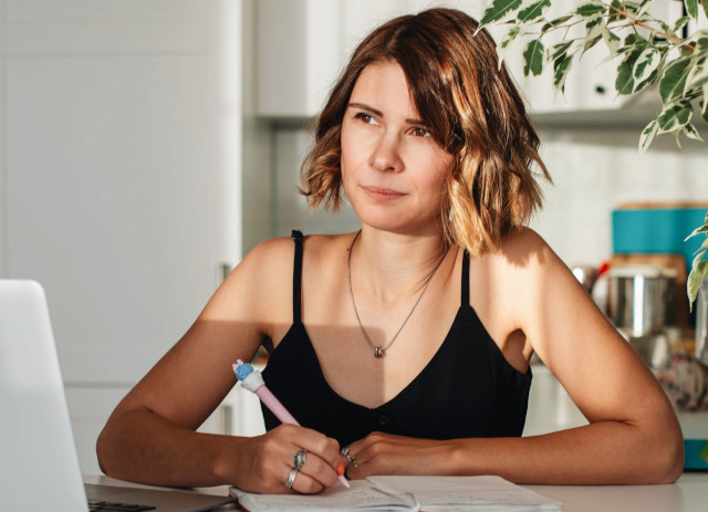 Mulher jovem de cabelo ondulado, castanho claro, pelos ombros, com t-shirt de alças pretas e a escrever sobre significado de gap year.