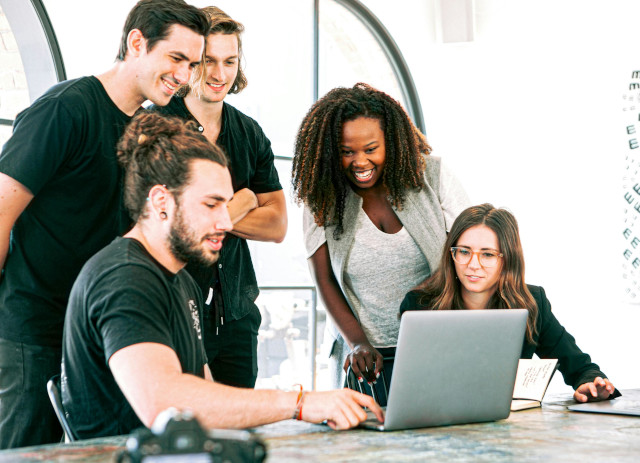 Três jovens homens vestidos de preto e duas jovens mulheres a sorrirem e a olharem para um computador portátil enquanto pesquisam cursos com futuro.