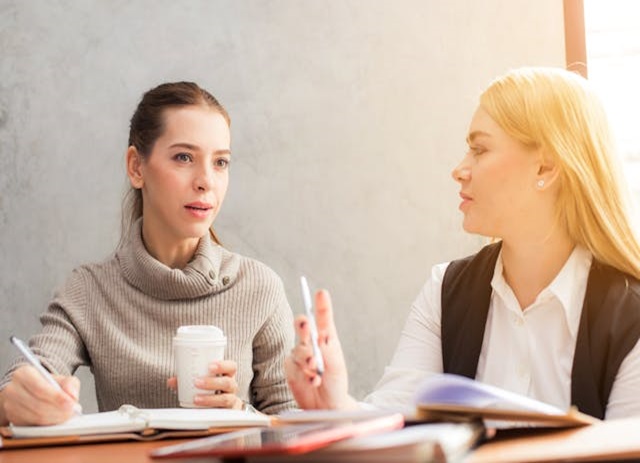 duas profissionais conversam sobre trabalho em mesa de reunião