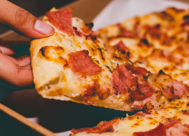 Mão a segurar uma fatia de pizza.