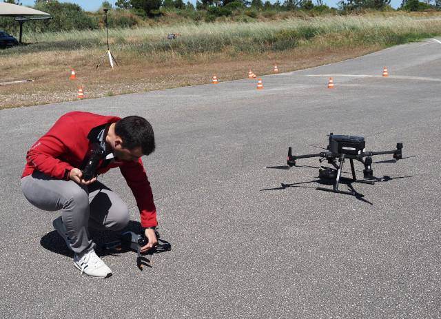 Aluno de curso de piloto de drones manipula um UAV numa estrada de asfalto.